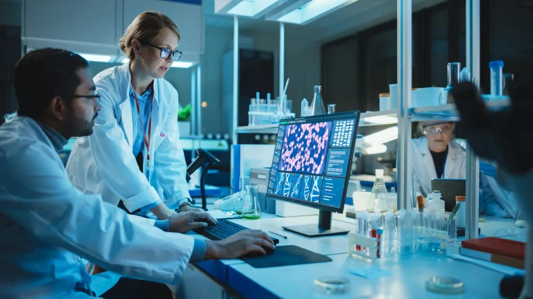 Two scientists in lab coats reviewing cell analysis data on a computer monitor in a modern laboratory at night